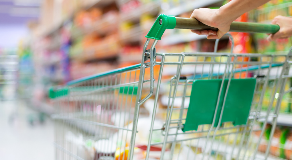 A close-up of a person pushing a shopping trolley down an aisle in a supermarket.