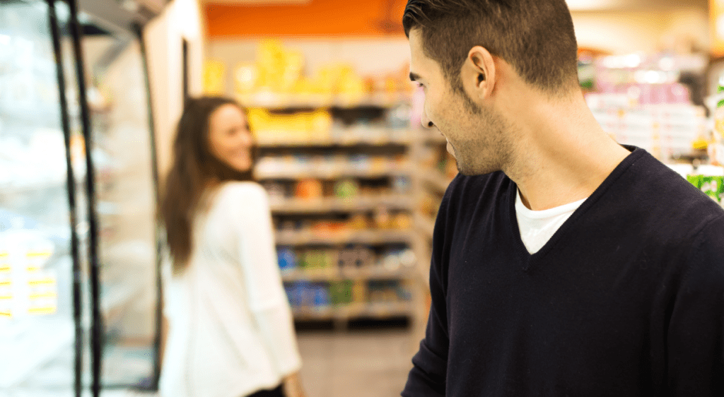 A man glancing back at a woman in the supermarket aisle, suggesting a potential romantic connection.