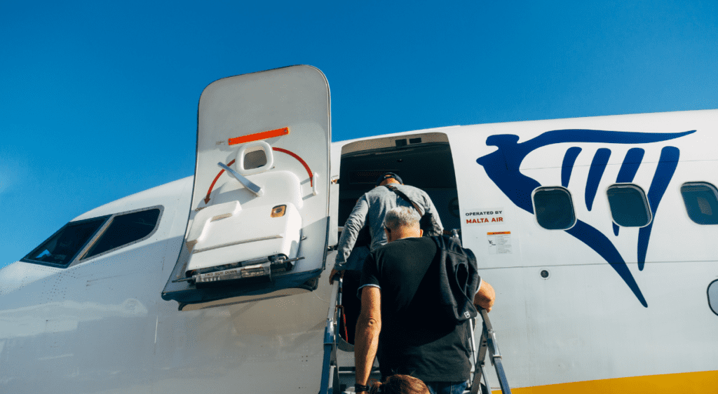 nterior view of a Ryanair airplane with passengers seated and a flight attendant walking down the aisle.