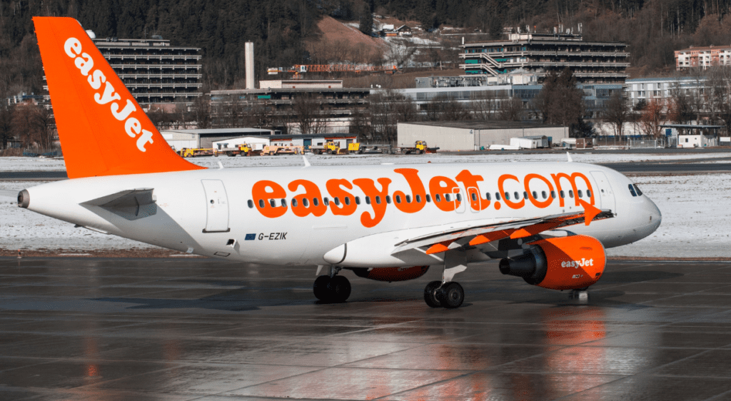 easyJet airplane on an airport tarmac with surrounding snow-covered landscape and buildings in the background.